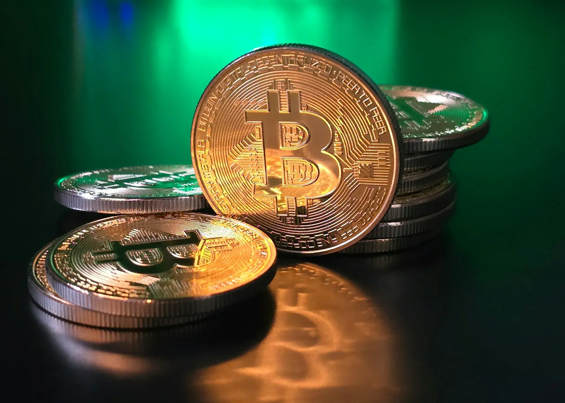 A stack of gold and silver Bitcoin coins on a reflective black surface.