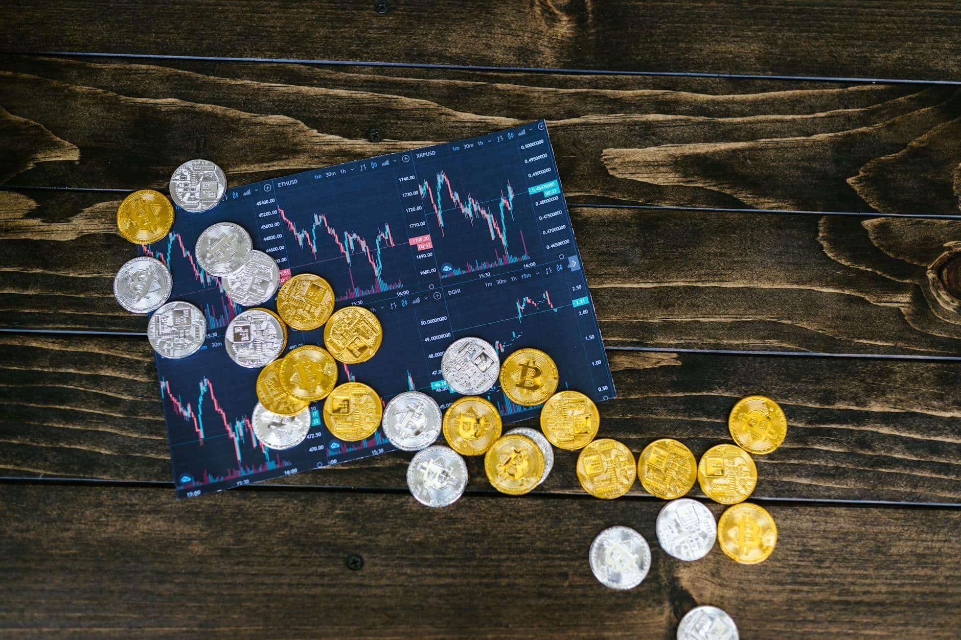 Gold and silver cryptocurrency coins on a market performance chart on a wooden surface.