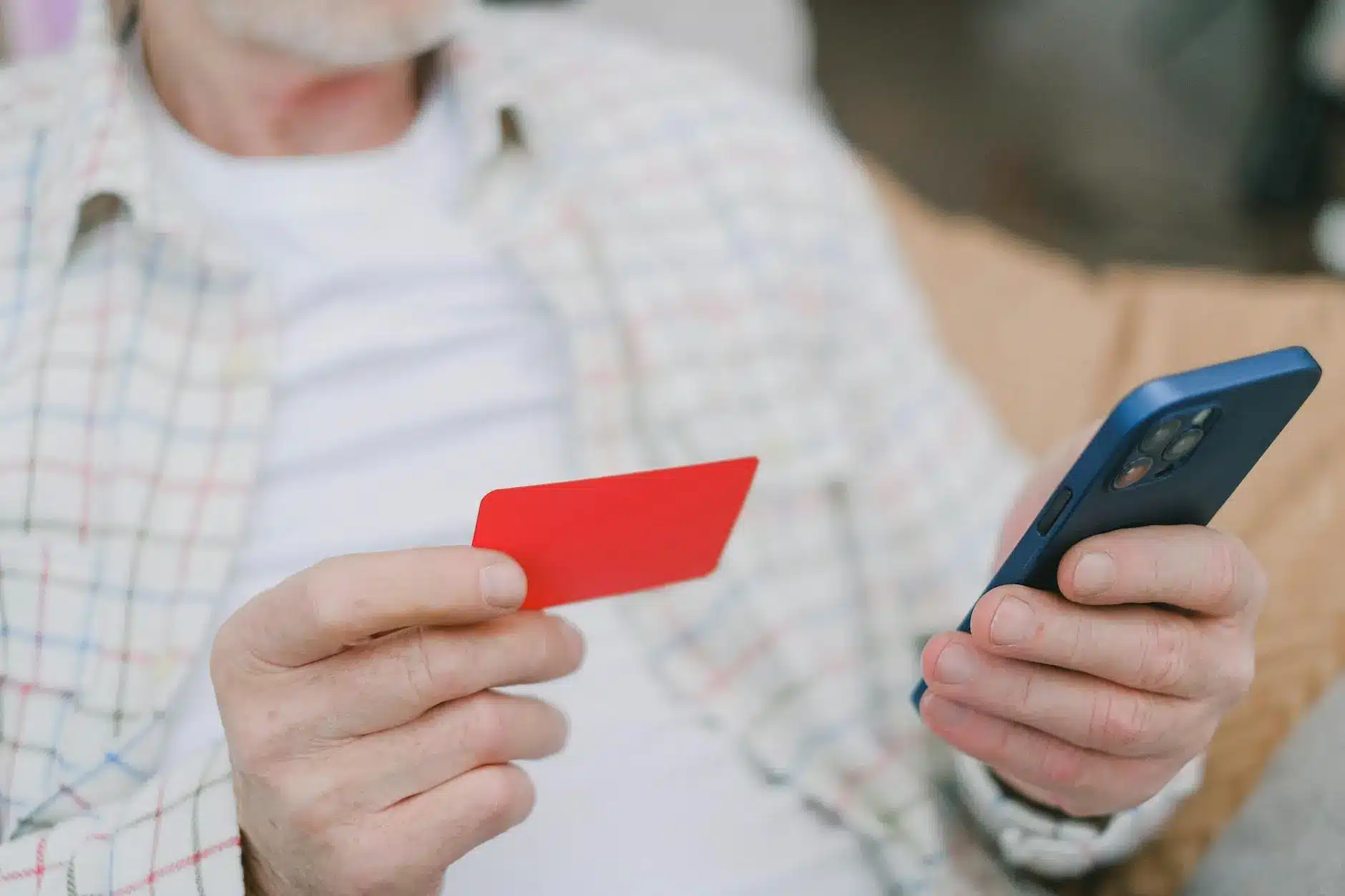 An older man holds a red card in one hand and a smartphone in the other, seated indoors.