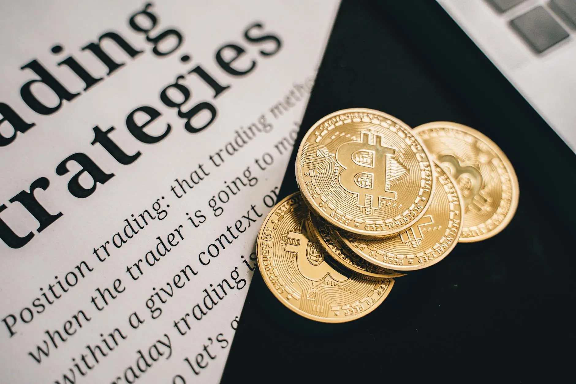 Three gold Bitcoin coins on a paper discussing trading strategies and a laptop.