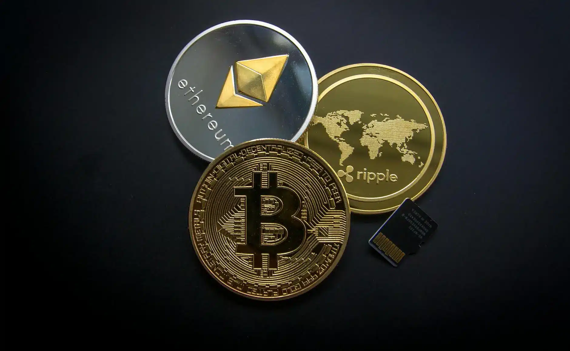 Three cryptocurrency coins: Bitcoin, Ethereum, and Ripple, with a memory card on a dark background.