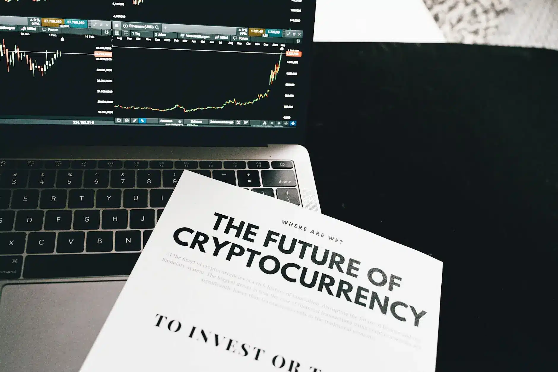 A laptop displaying cryptocurrency charts and a book titled 'The Future of Cryptocurrency'.