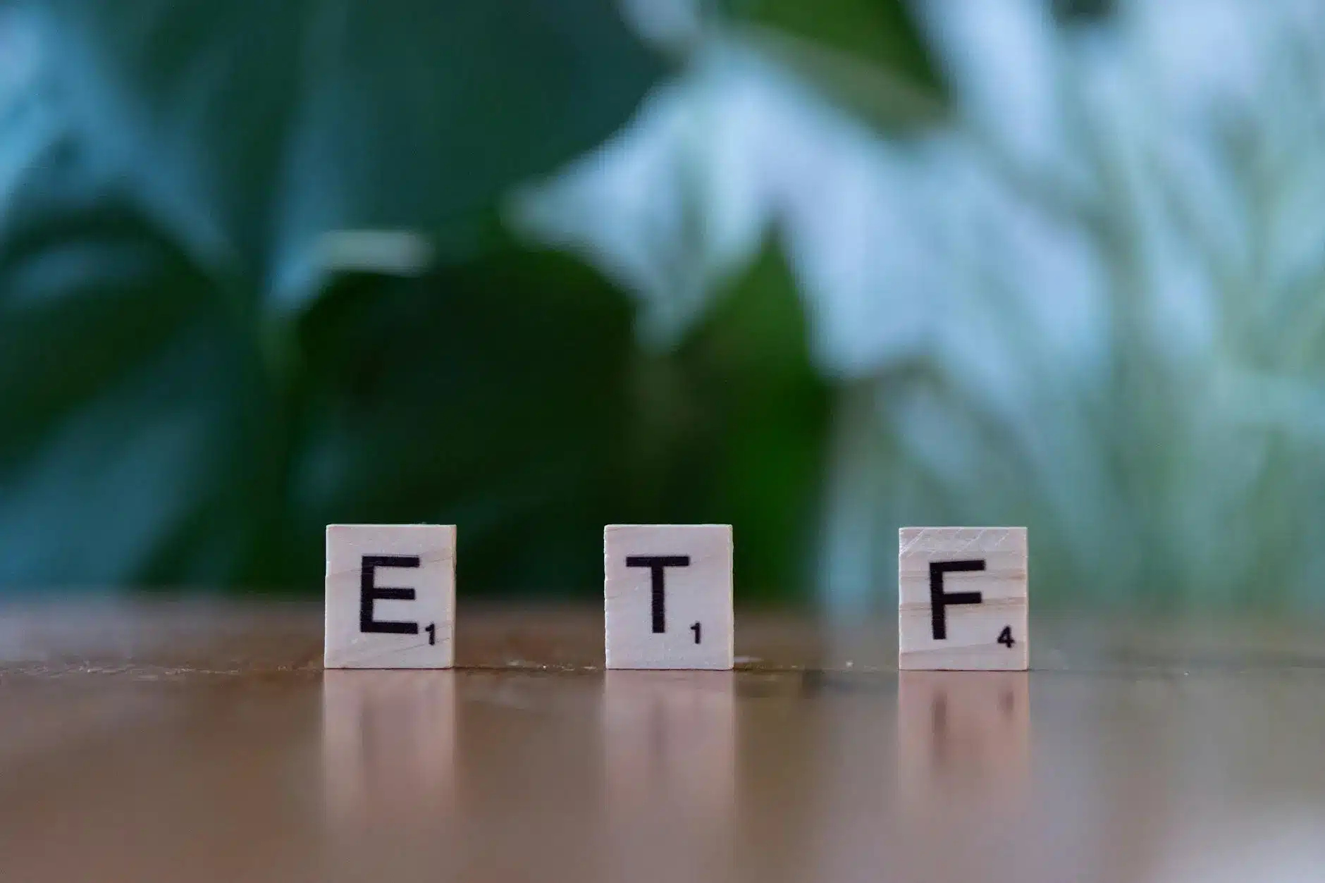 Three wooden letter tiles spell 'ETF' on a wooden surface with a blurred green background.
