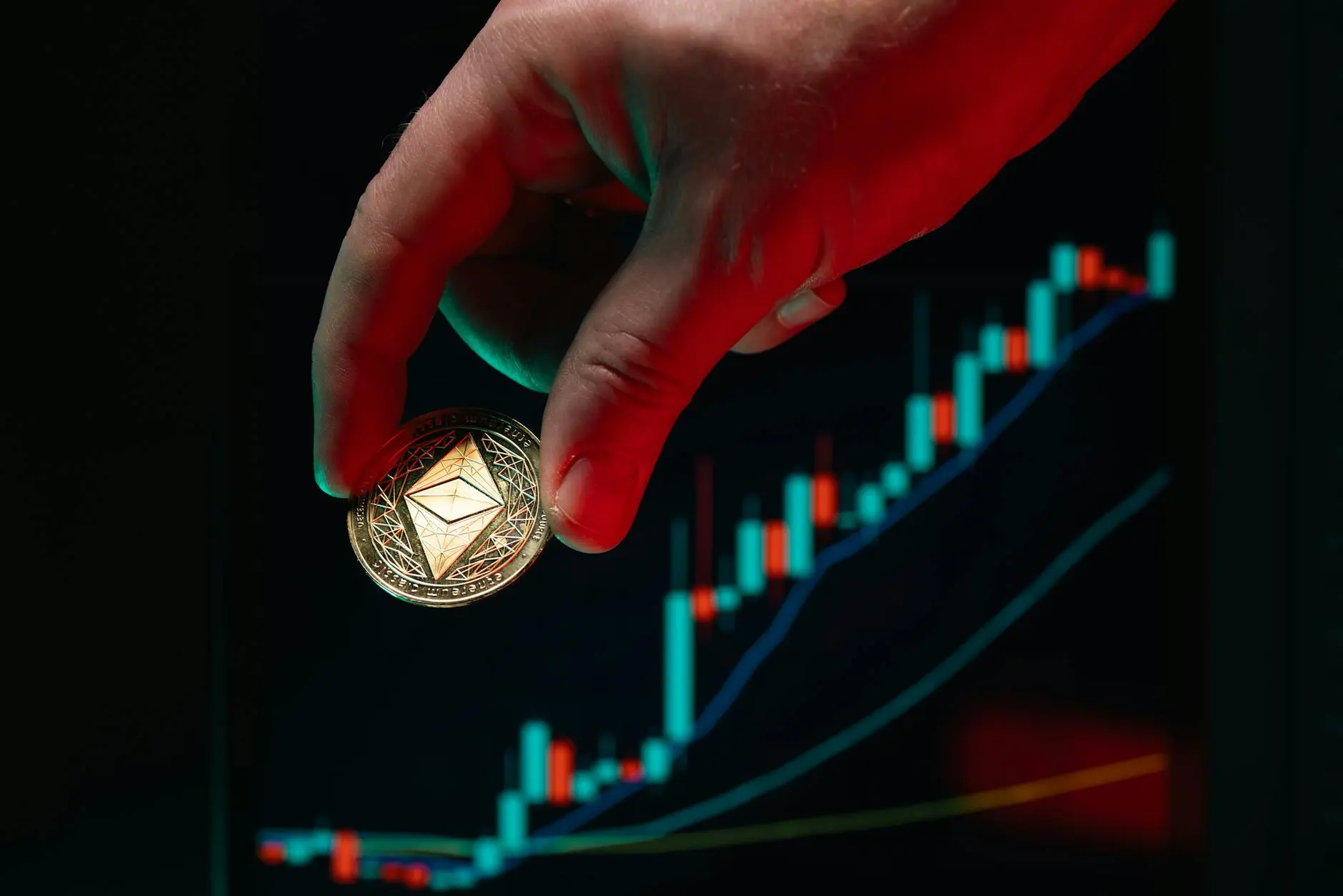 Hand holding a gold Ethereum coin in front of a price chart background.