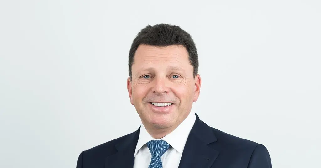 Smiling man in a suit with short hair against a plain background.