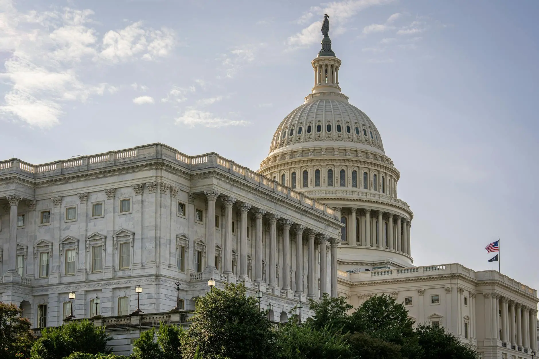 The U.S. Capitol building with its dome and American flag under a clear sky.