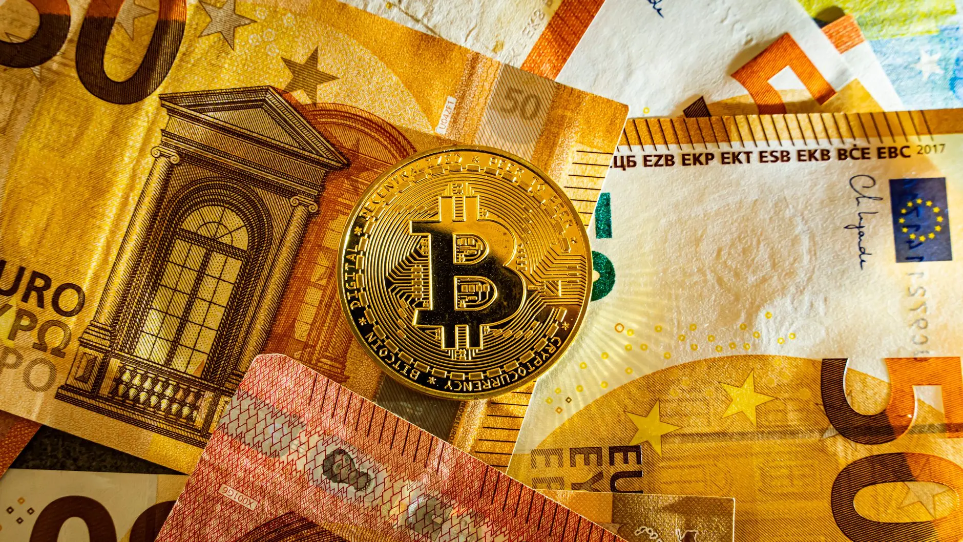 A Bitcoin coin on top of various Euro banknotes.