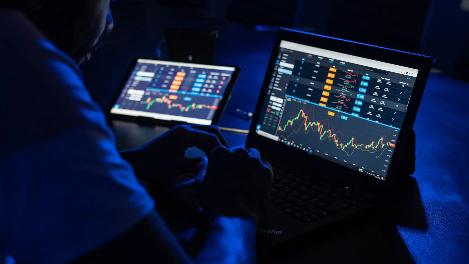 Trader analyzing stock charts on multiple screens at night.