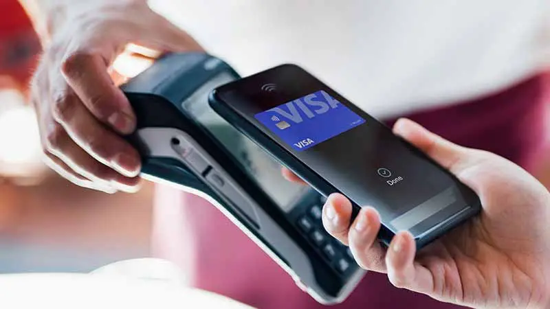 A person using a smartphone with a Visa digital wallet to make a contactless payment at a credit card terminal