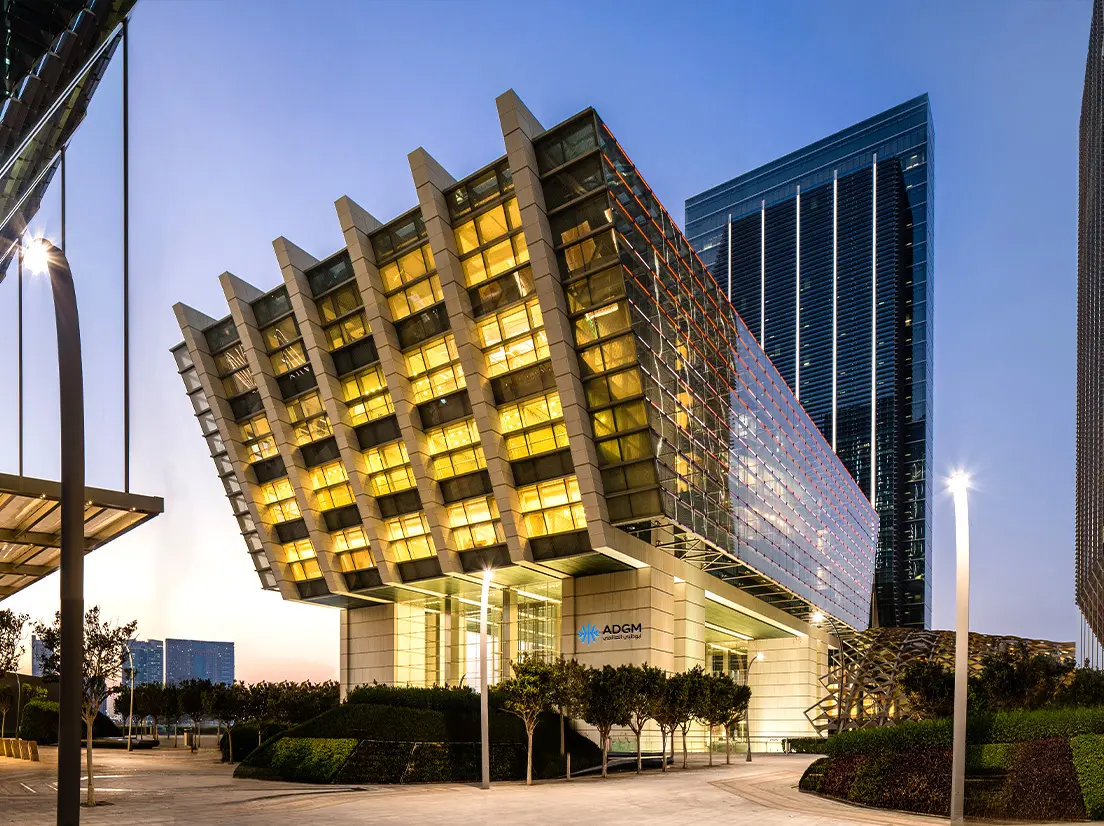 Modern architectural building of the Abu Dhabi Global Market (ADGM) with illuminated golden windows at dusk.