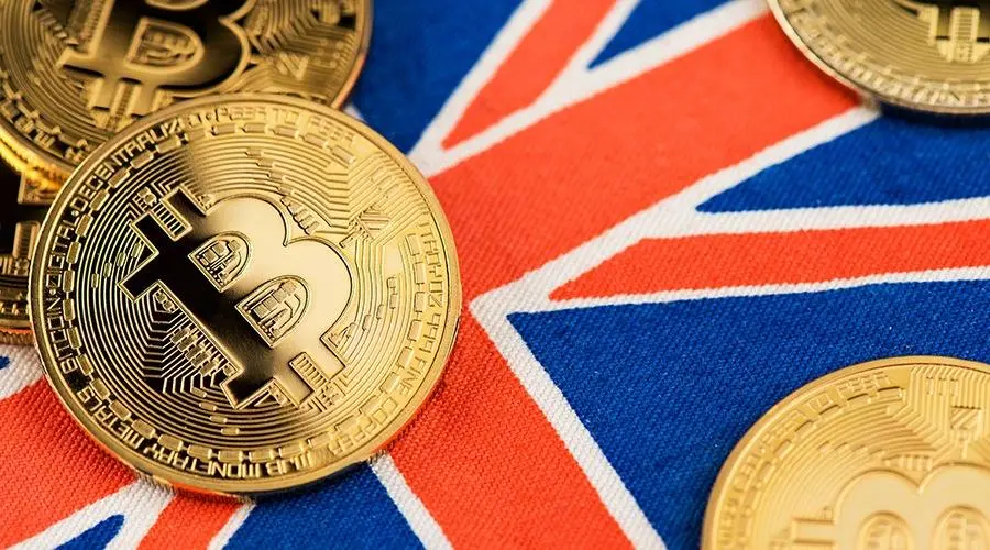 Physical gold Bitcoin coins scattered across the fabric of the Union Jack British flag.