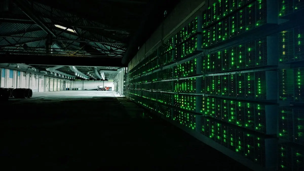Rows of cryptocurrency mining rigs with glowing green LED indicators in a large industrial warehouse