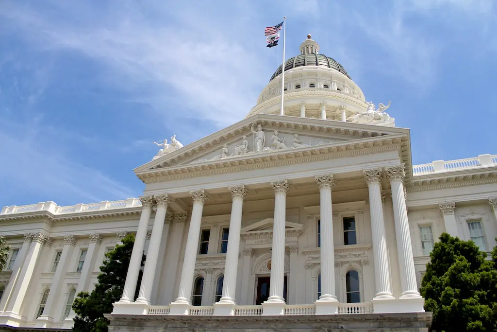 The white neoclassical architecture of the California State Capitol building with its dome and US flag.