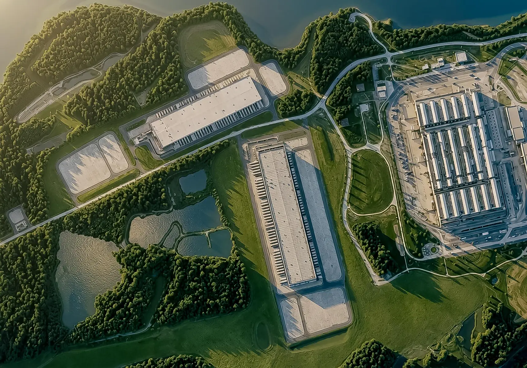 Aerial view of a large industrial complex with white warehouses surrounded by green forests and ponds