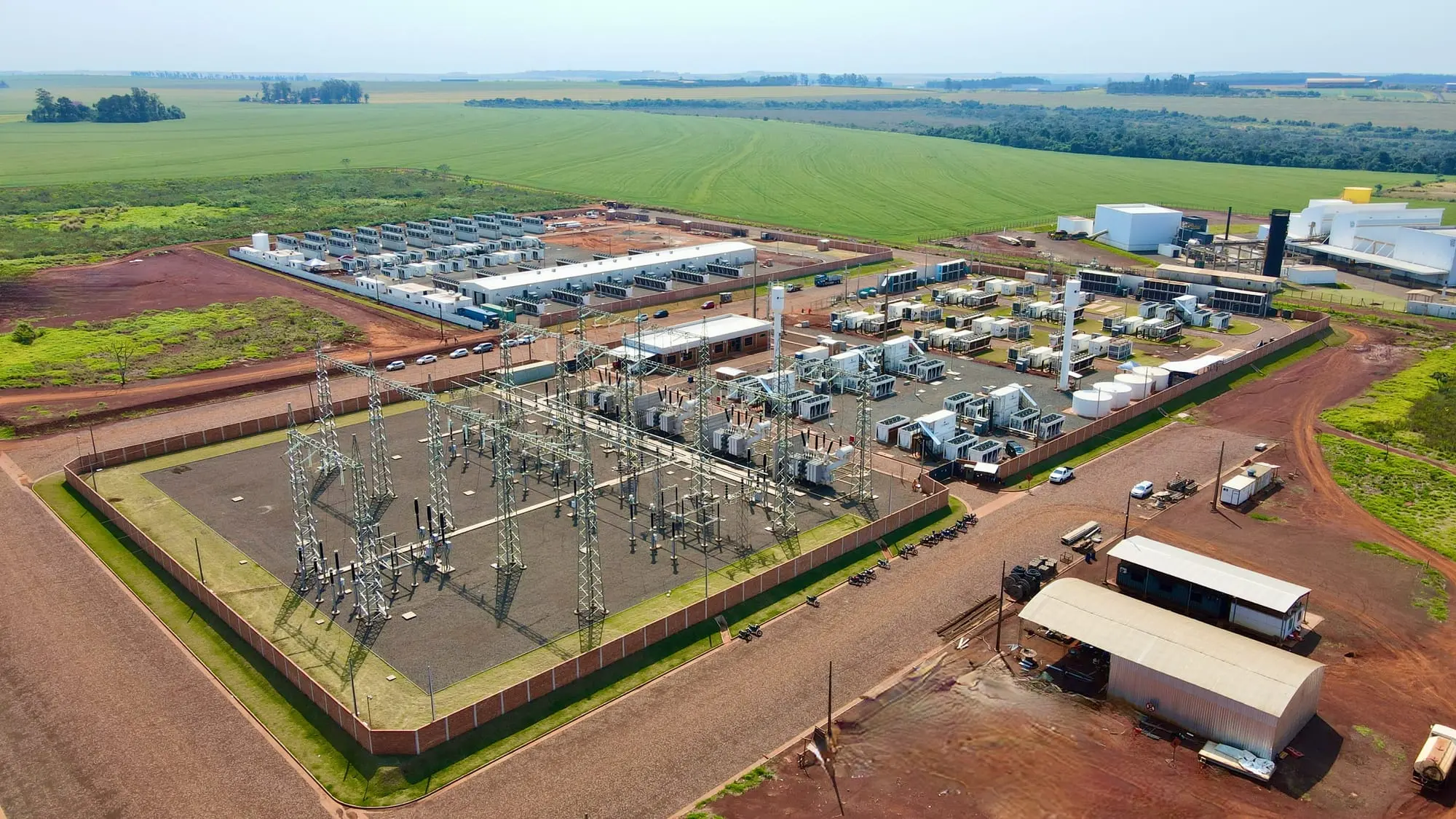 Aerial view of a large industrial bitcoin mining facility with a power substation and containerized miners.