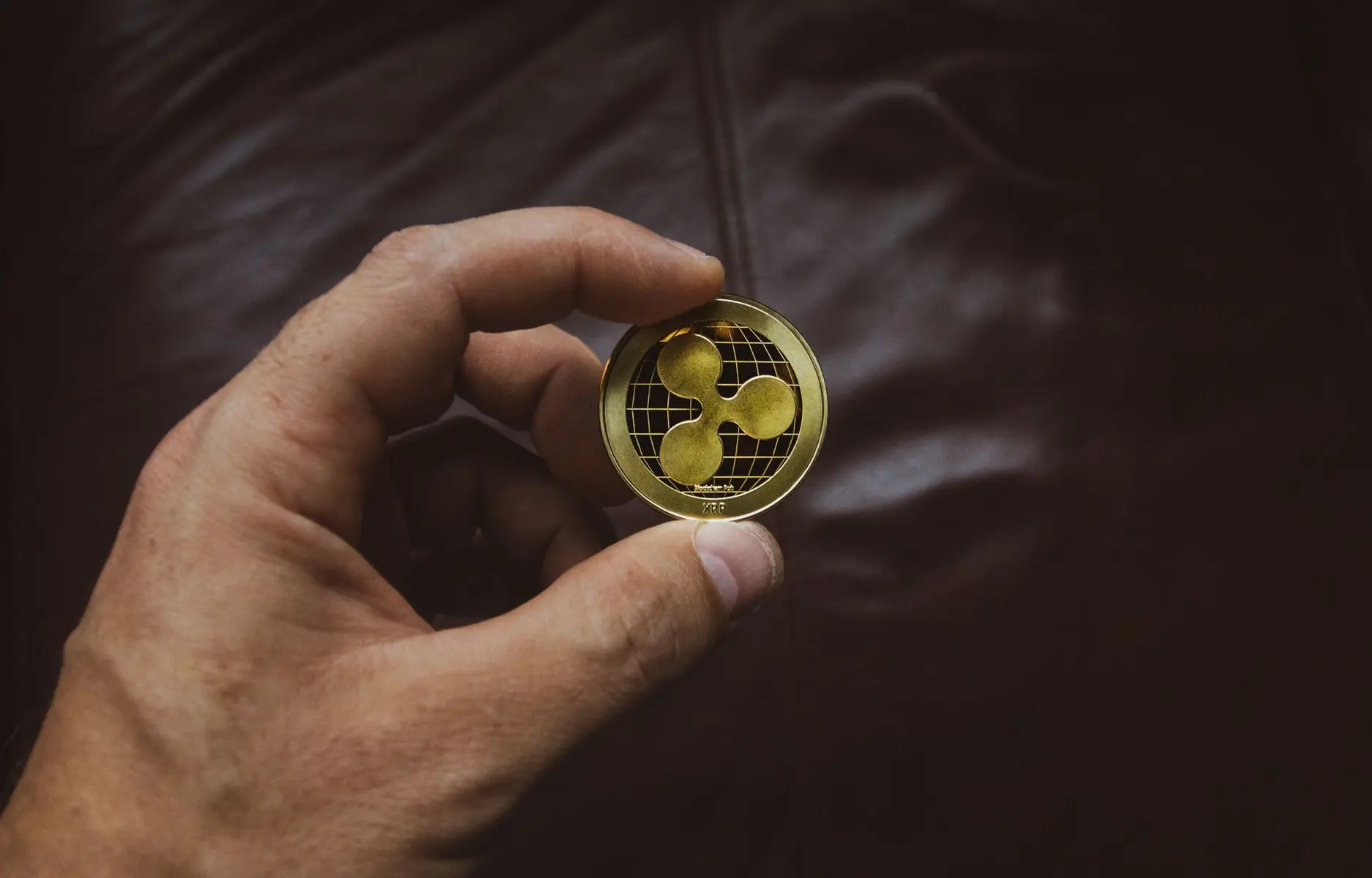 A person holding a gold physical Ripple XRP cryptocurrency coin featuring the three-dot logo