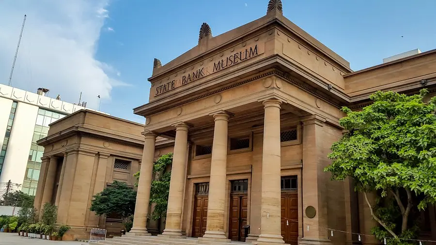 The sandstone exterior of the State Bank of Pakistan Museum in Karachi with large columns and a clear blue sky.