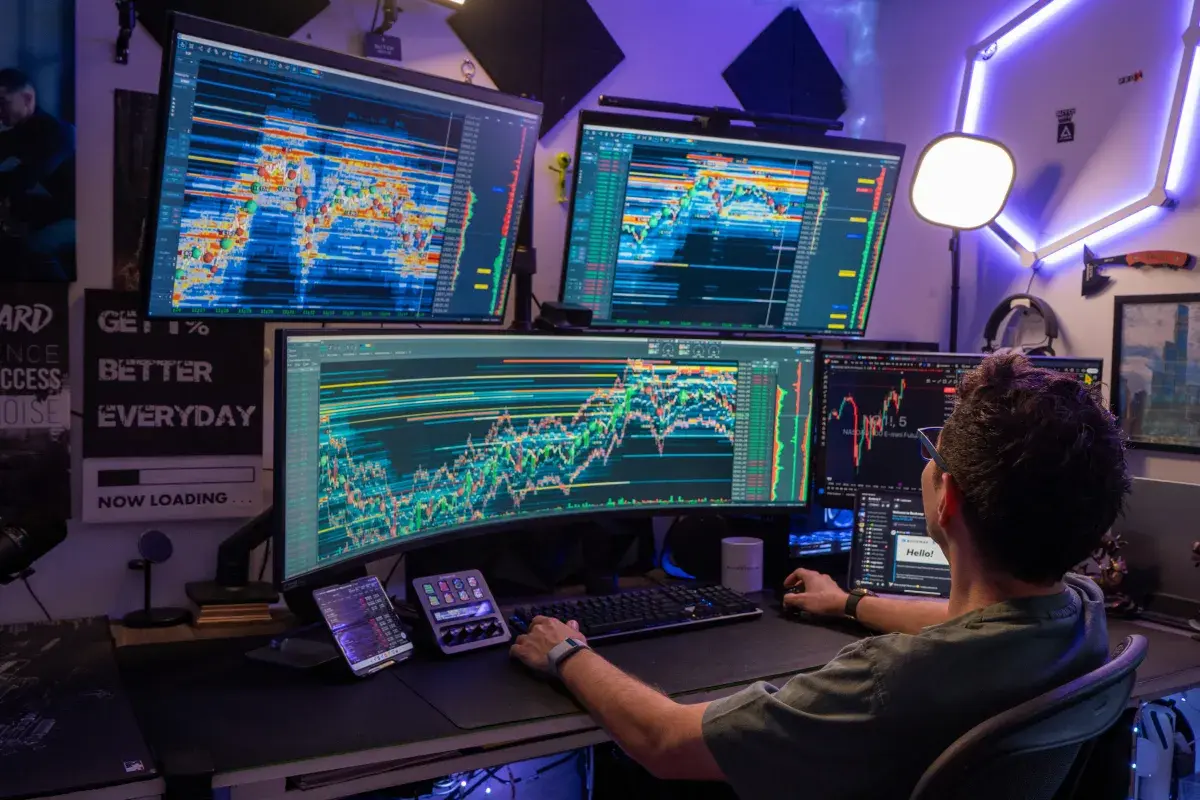 A trader using a multi-monitor setup displaying complex stock market candlestick charts and technical indicators