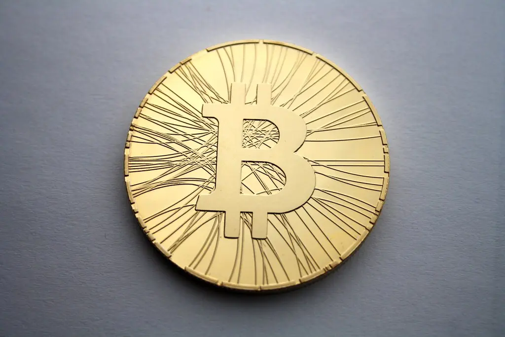 Eine physische goldfarbene Münze mit dem Bitcoin-Symbol auf einem hellblauen Hintergrund.