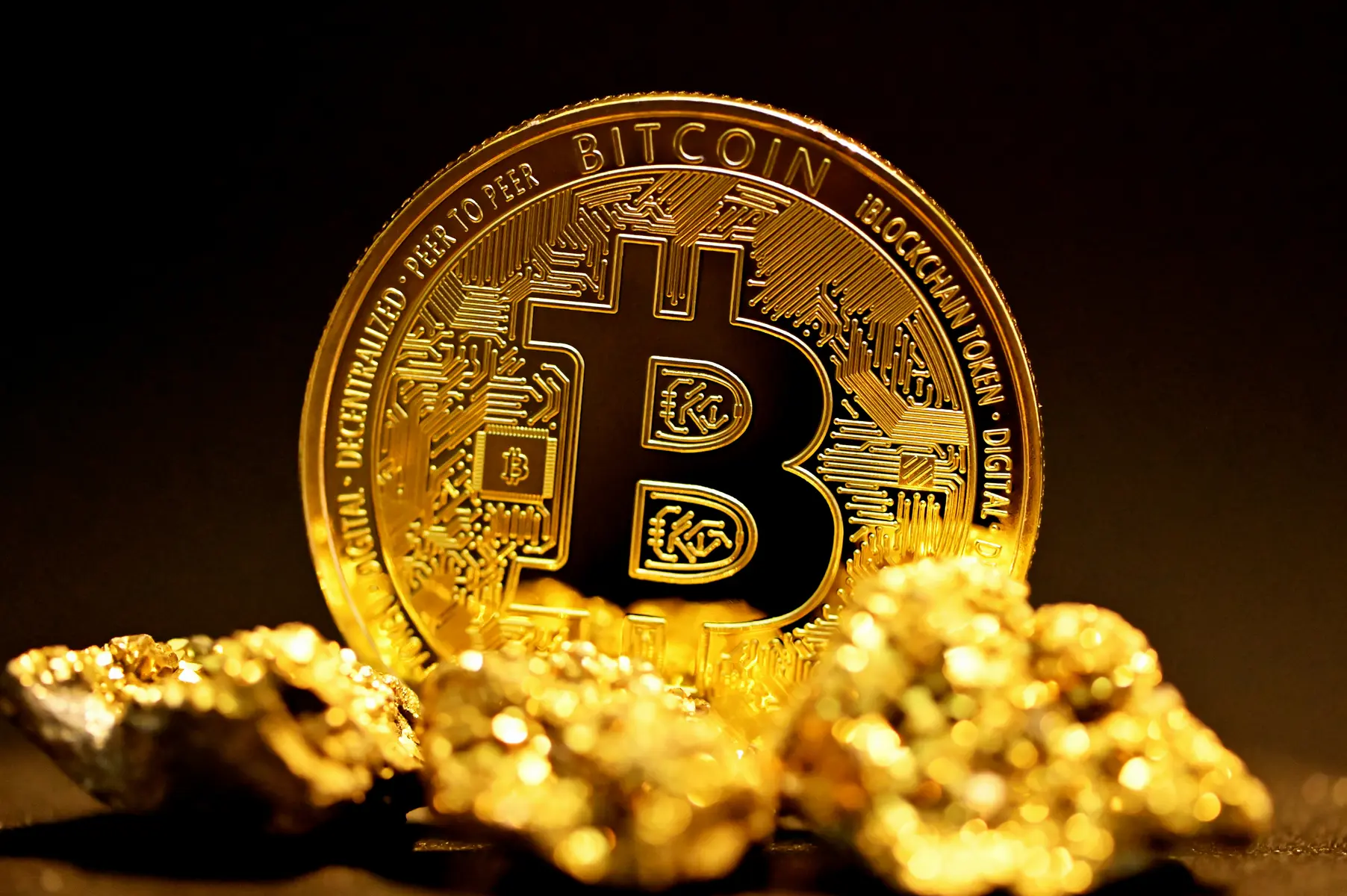 Eine goldene Bitcoin-Münze auf einem Haufen aus Goldnuggets vor schwarzem Hintergrund.
