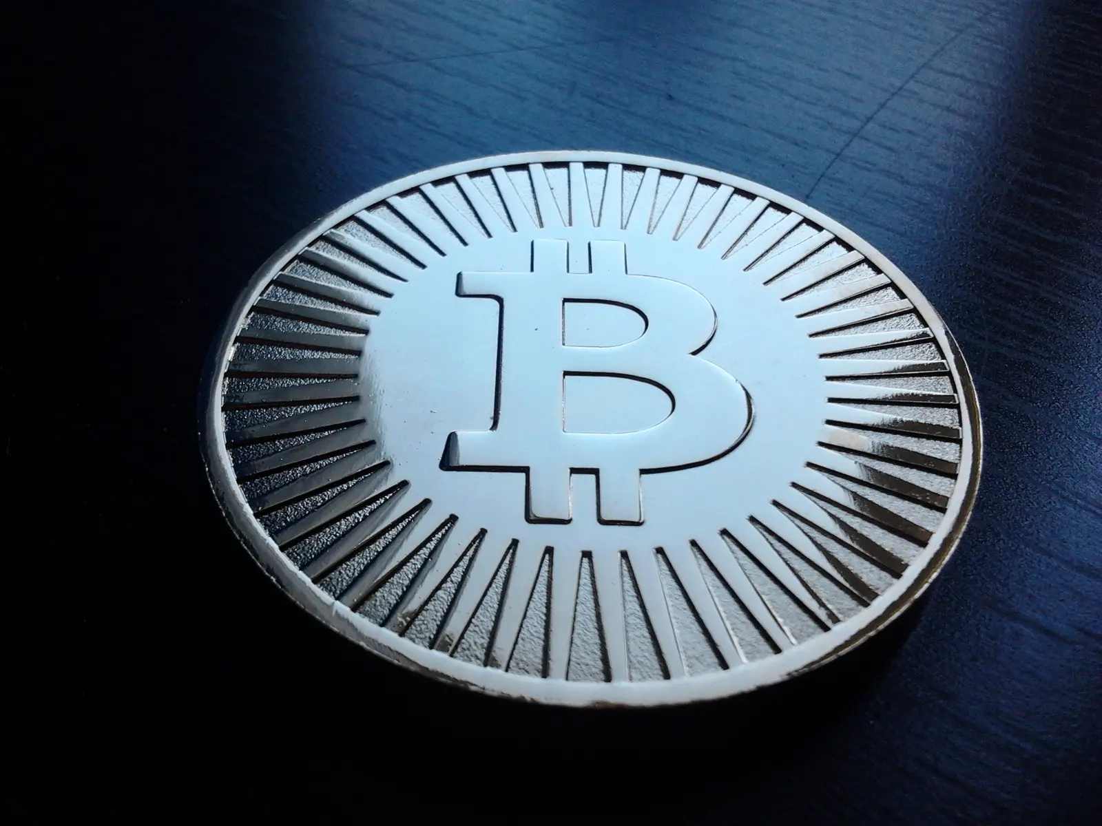 Eine physische Bitcoin-Gedenkmünze mit dem charakteristischen B-Symbol auf dunklem Untergrund.