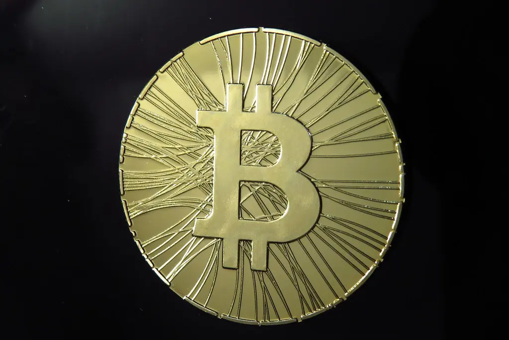 Eine goldfarbene physische Bitcoin-Münze vor einem schwarzen Hintergrund.