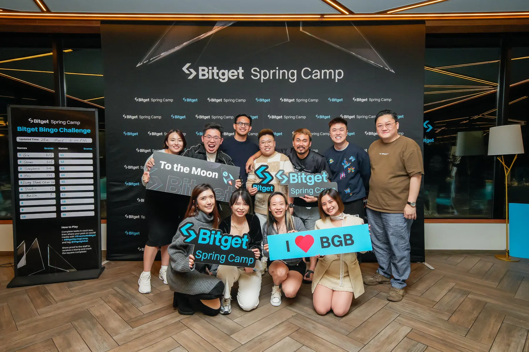 Eine Gruppe von Menschen posiert vor einer Bitget Spring Camp Wand mit verschiedenen Bitget-Schildern.