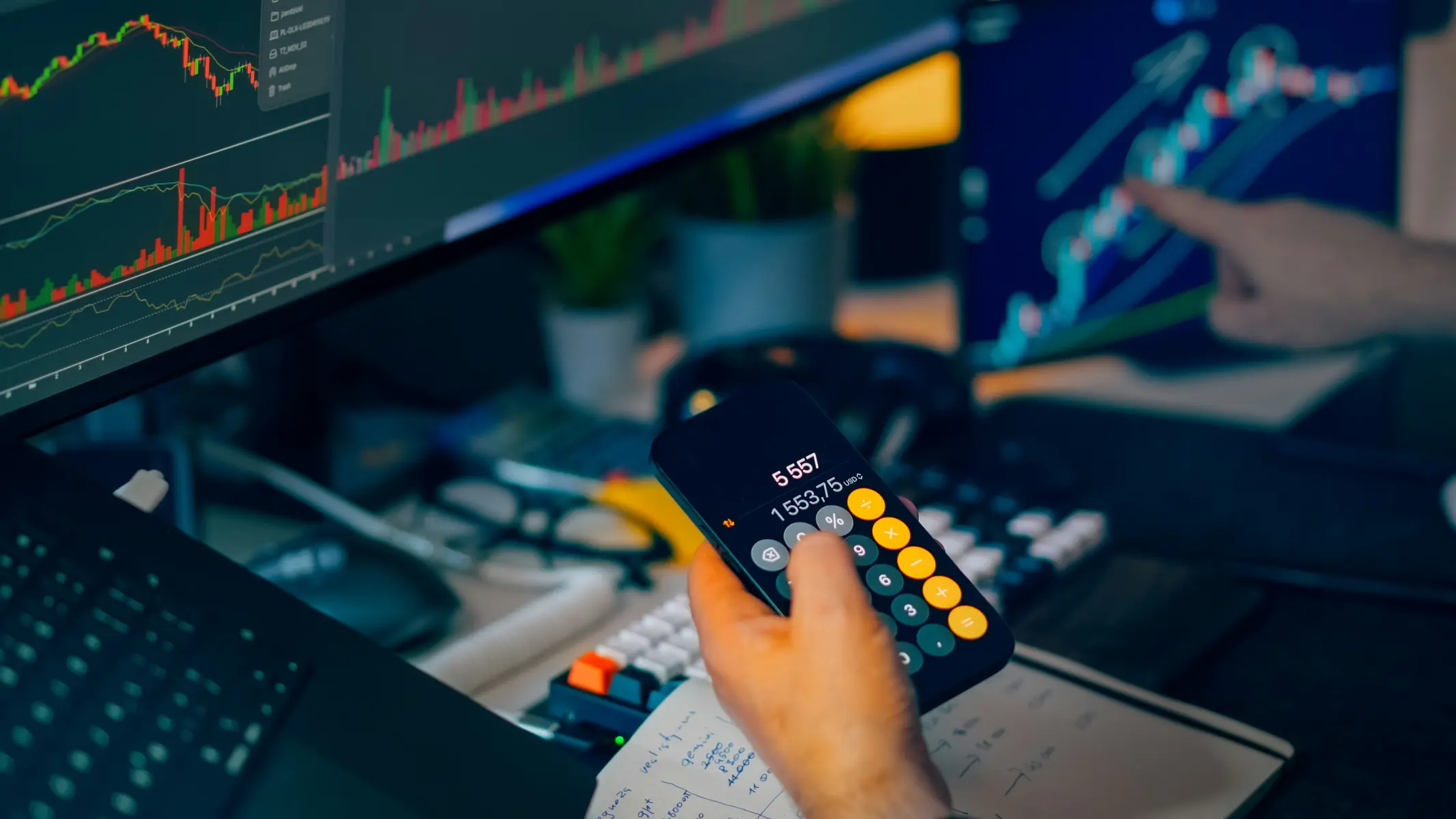 Nahaufnahme eines Smartphones mit Taschenrechner-App vor mehreren Monitoren mit Krypto-Kurscharts.