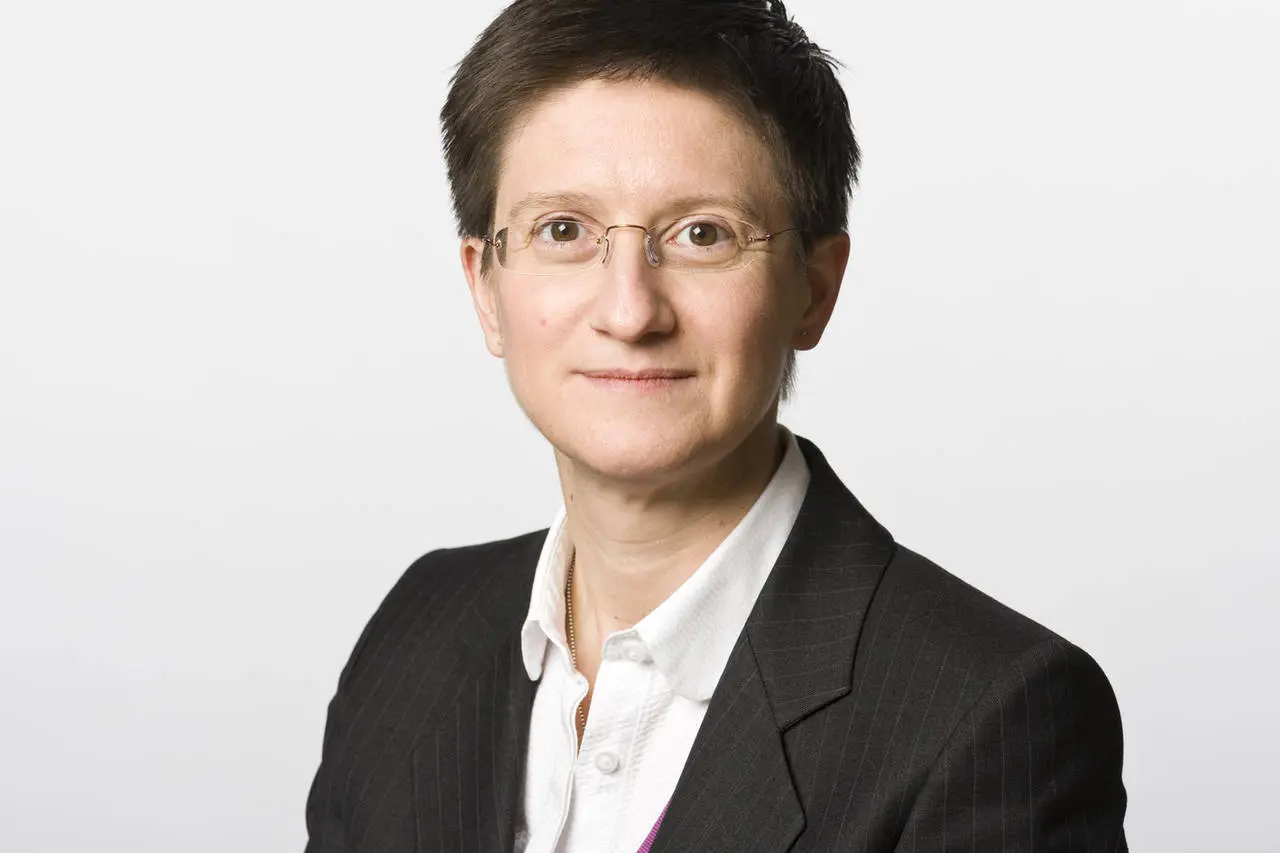 Headshot of Julia Hoggett, wearing glasses and a dark pinstripe suit jacket over a white shirt.