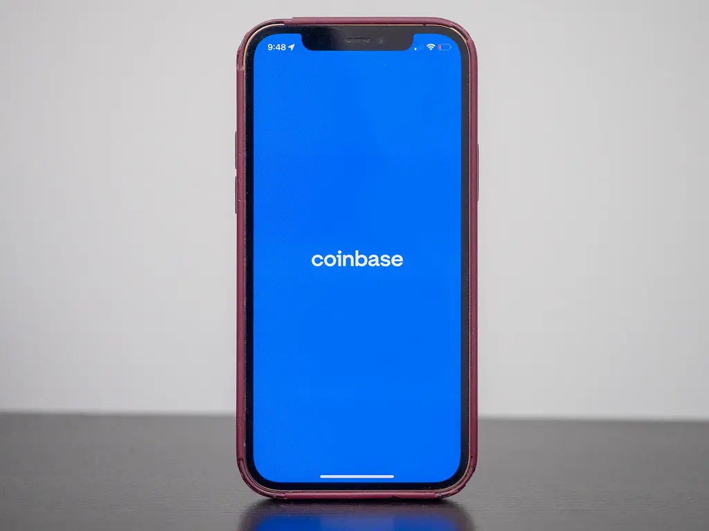 Die Coinbase-App auf einem Smartphone mit blauem Hintergrund und weißem Logo.
