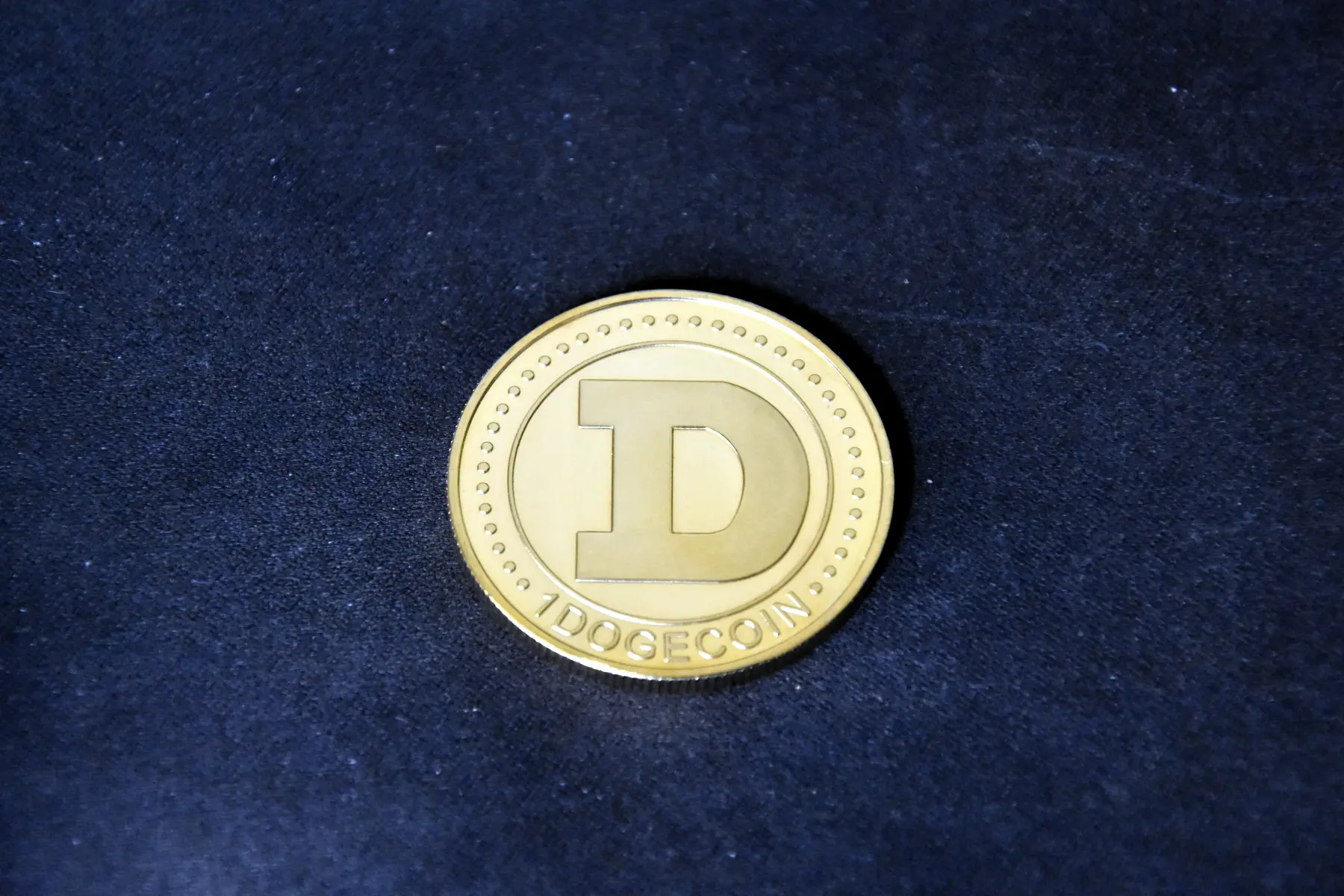 Eine goldfarbene Dogecoin-Münze mit einem großen 'D' auf einem schwarzen Hintergrund.