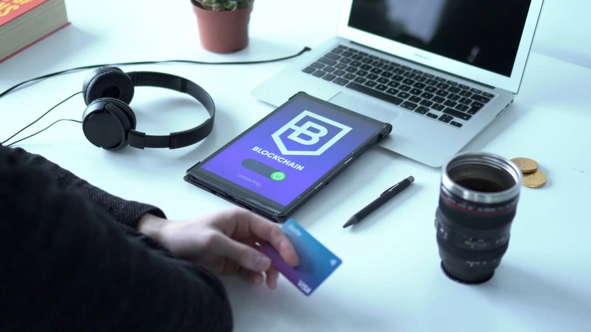 A person holding a credit card next to a tablet displaying a blockchain interface.