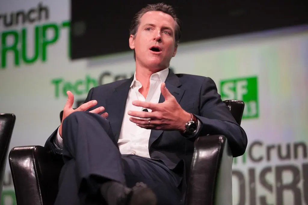Gavin Newsom spreekt tijdens een evenement, zittend in een zwarte leren stoel.