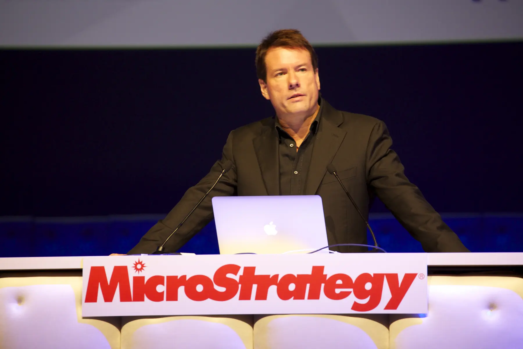 Michael Saylor spreekt tijdens een keynote presentatie achter een podium met het logo van MicroStrategy.