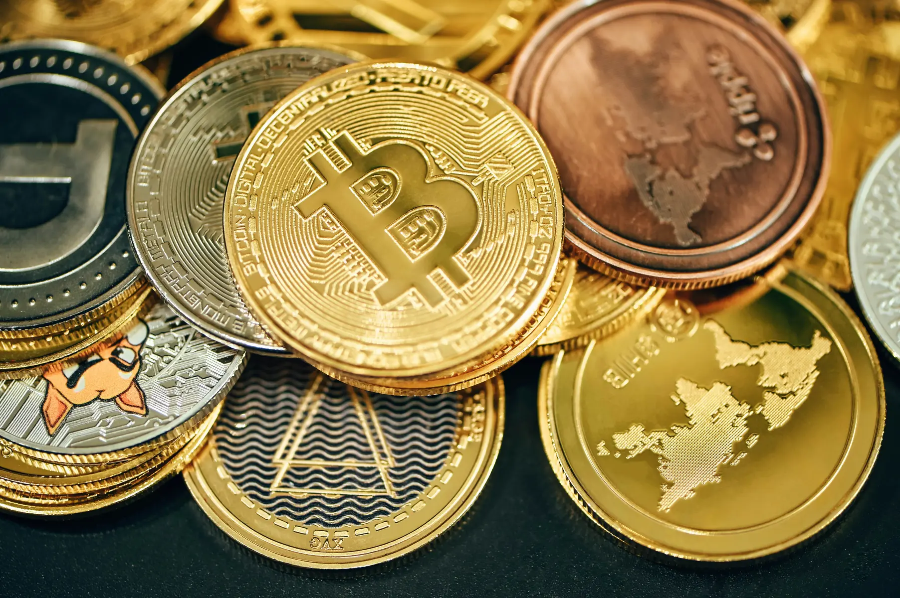 Een verzameling fysieke cryptomunten, waaronder Bitcoin en Ripple, op een zwarte achtergrond.