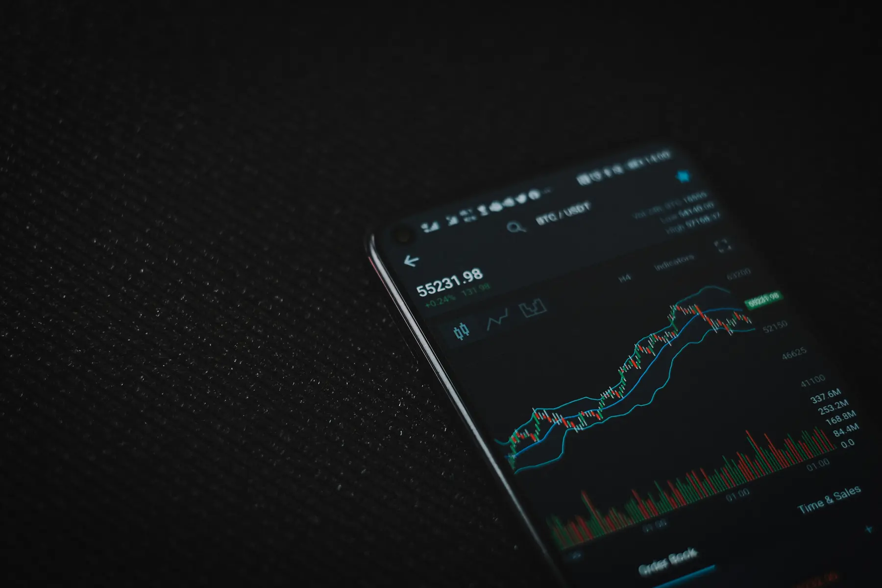 Een smartphone die cryptocurrency handelsgrafieken en koersen weergeeft op een zwarte achtergrond