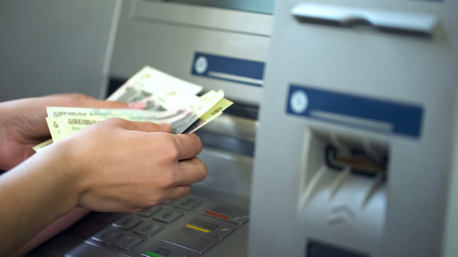 A person’s hands counting Russian ruble banknotes they have just withdrawn from an ATM.