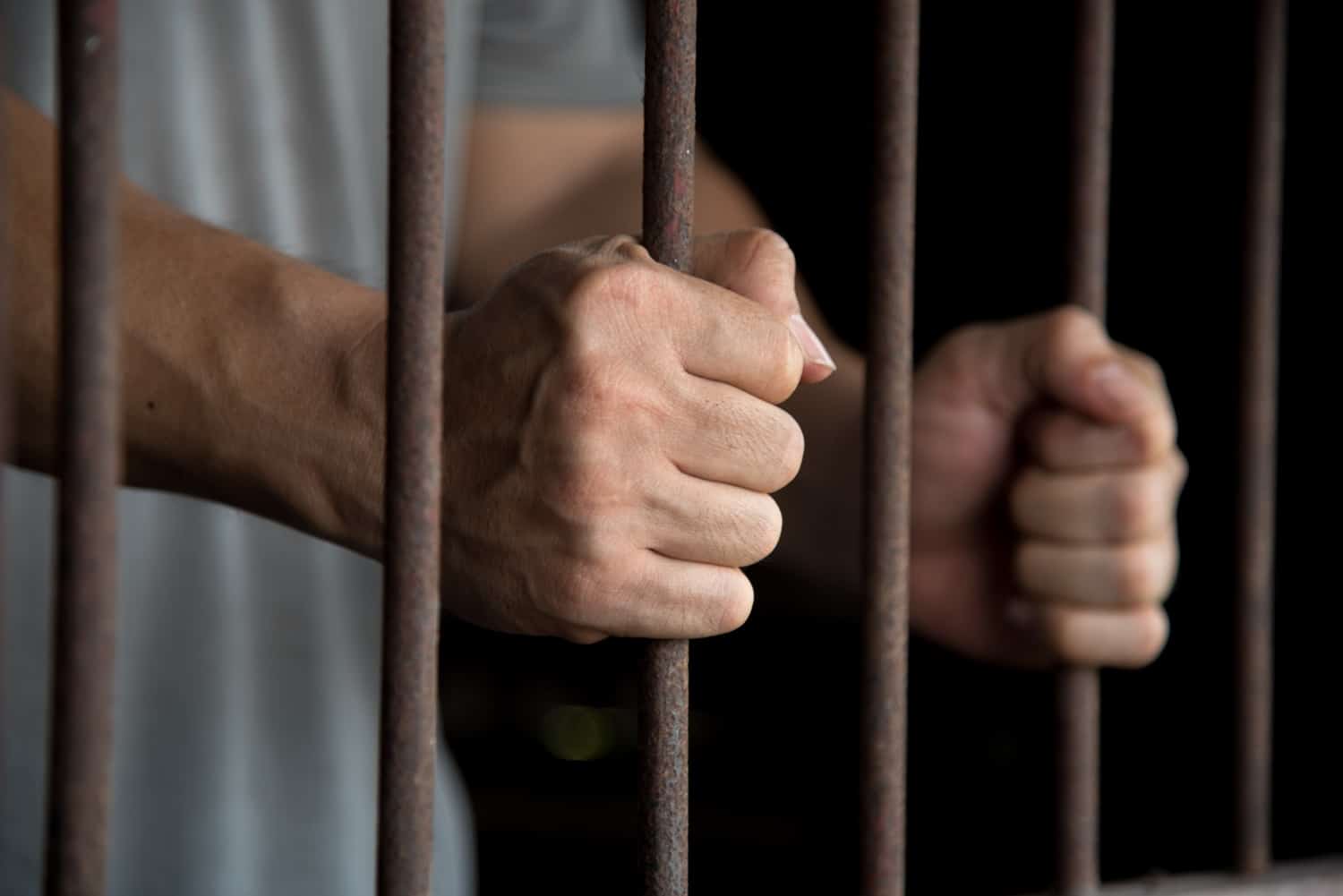 The hands of a prisoner in jail, holding onto their cell bars.