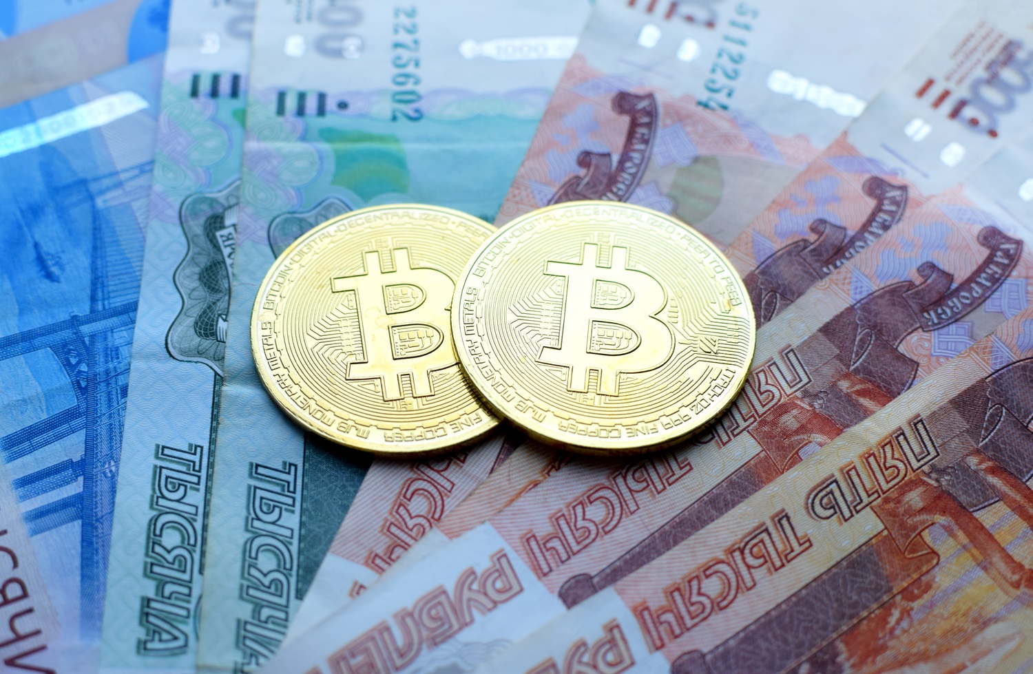 Metal tokens intended to represent Bitcoin rest on a selection of Russian ruble banknotes.