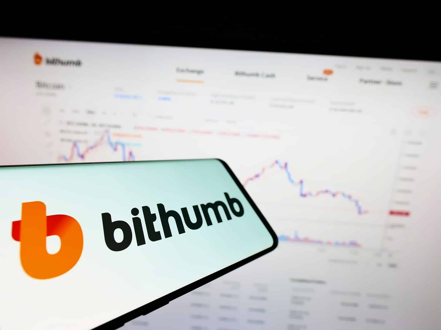A mobile phone displaying the logo of the South Korean crypto exchange Bithumb in front of a laptop screen.