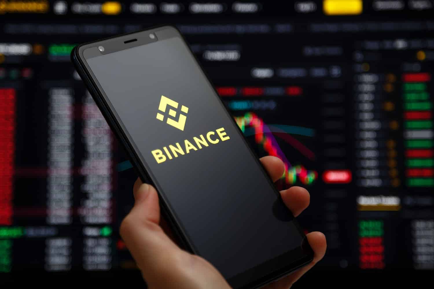 The Binance mobile app running on a smartphone screen with a trading page running on a laptop device in the background.