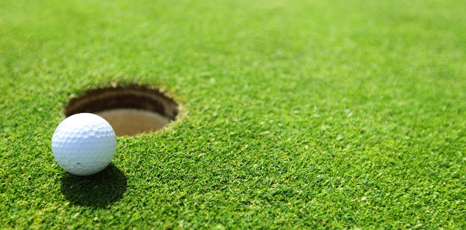 A golf ball on the lip of a cup on a green.