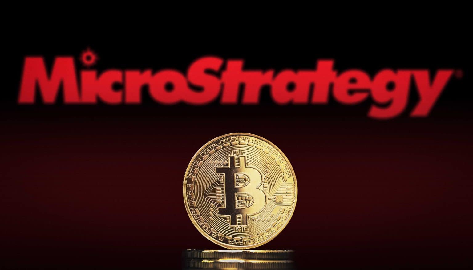 A Bitcoin coin sits in front of the MicroStrategy logo, representing the company's significant investment in Bitcoin.