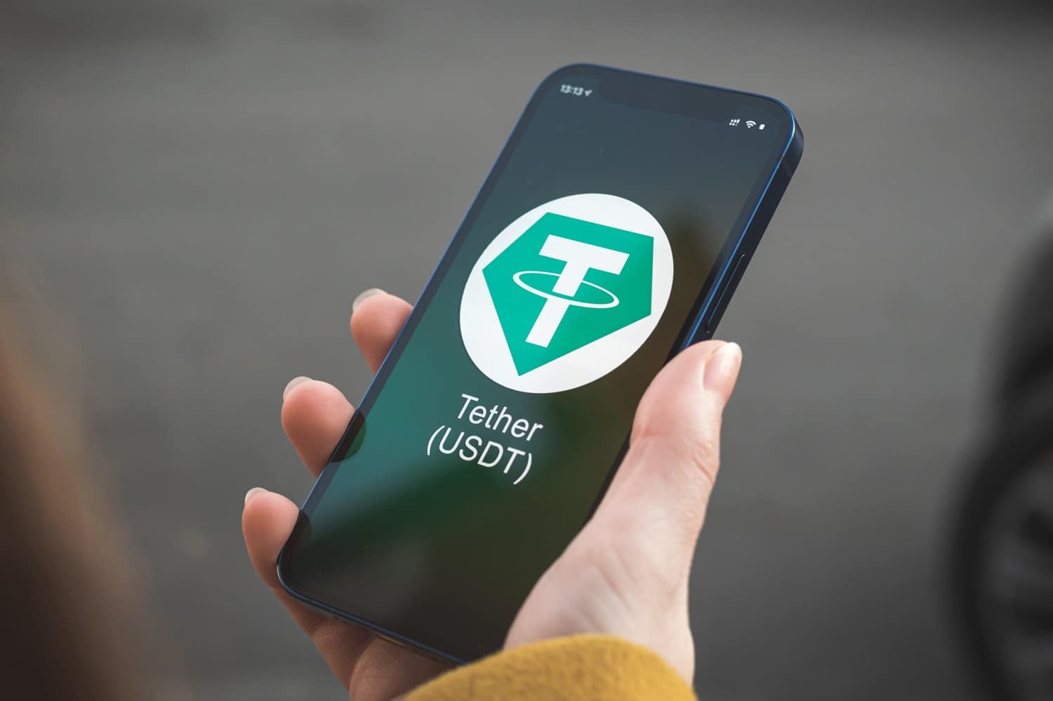 A person’s hand holds a smartphone with the Tether USDT cryptoasset symbol and logo on its screen.