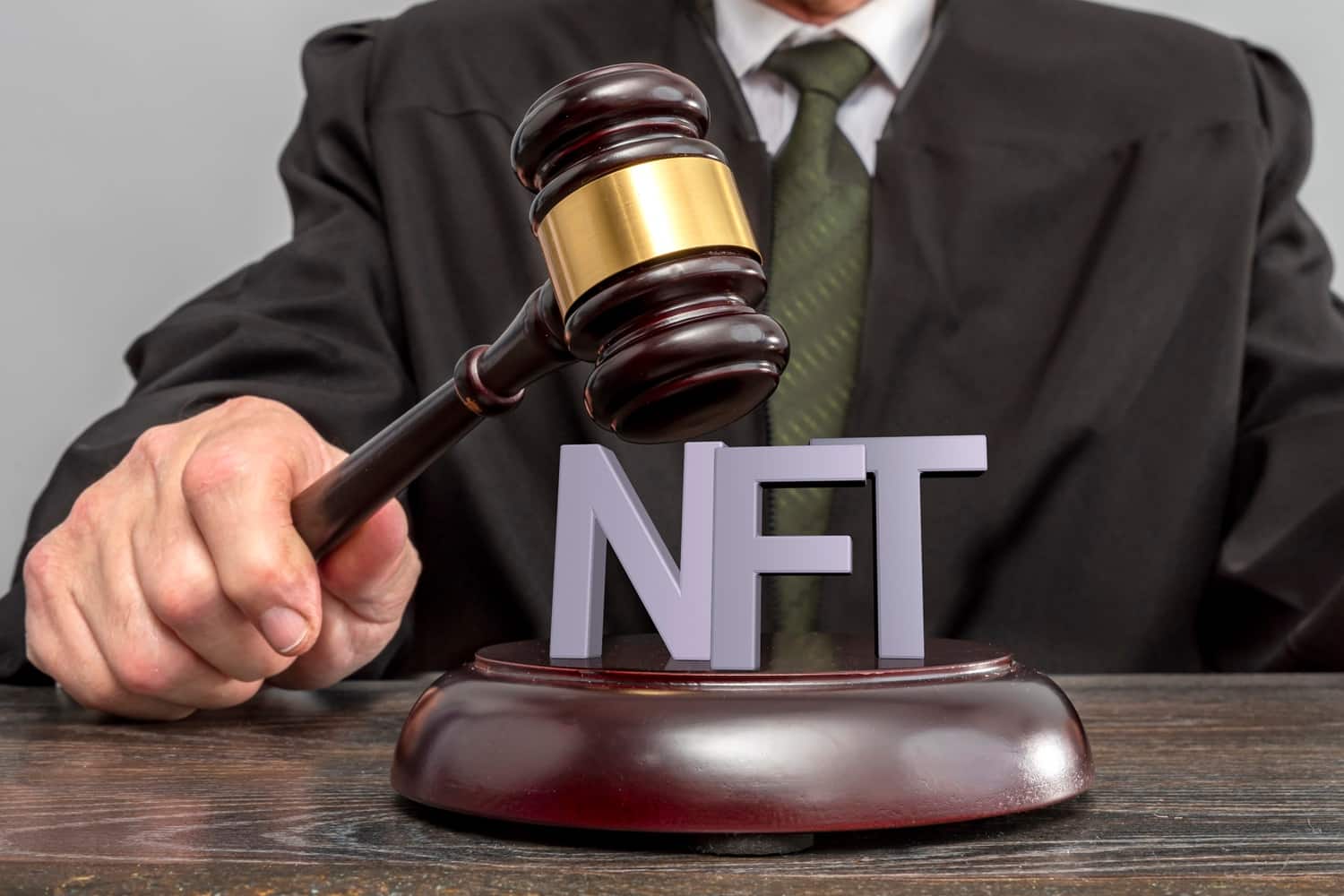 A judge strikes a block with a gavel. The letters NFT rest on the block.
