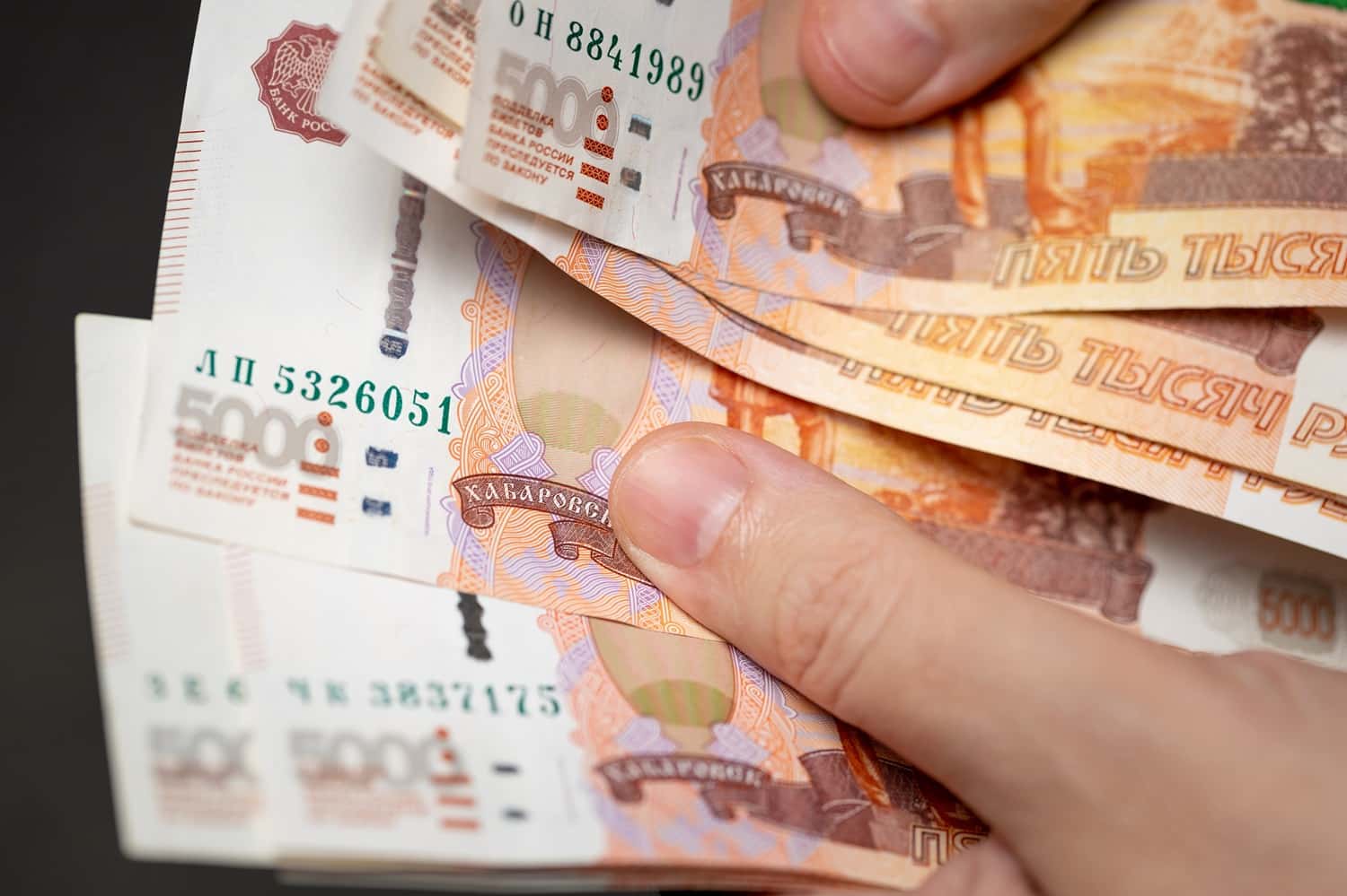 A person’s hands hold several five thousand Russian ruble banknotes.