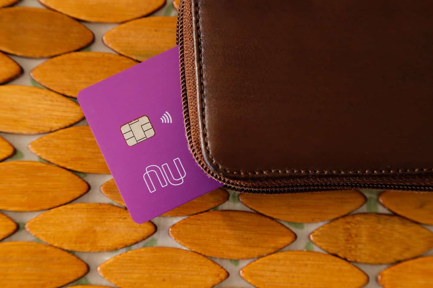 A Nubank bank card protrudes from a brown leather wallet.