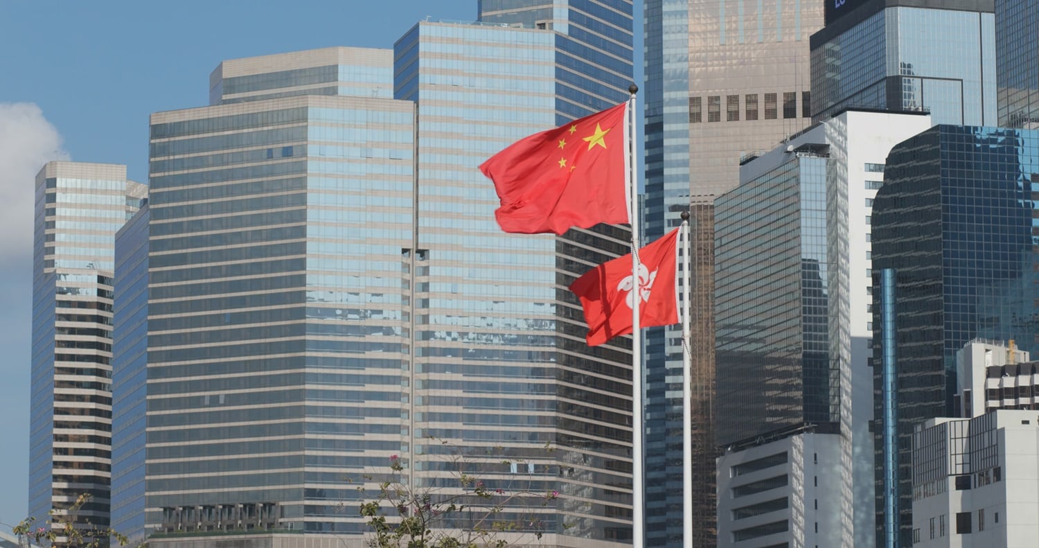 The flags of Hong Kong and China fly outside large office towers.