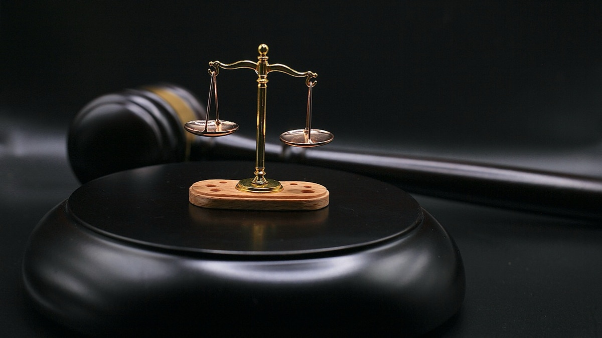صورةٌ لميزان العدالة موضوعاً على منصةٍ سوداء وخلفه مطرقة القاضي 