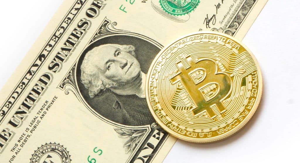 صورةٌ لعملة الدولار الأميركي وبجانبها عملةٌ ذهبيةٌ تحمل شعار بيتكوين